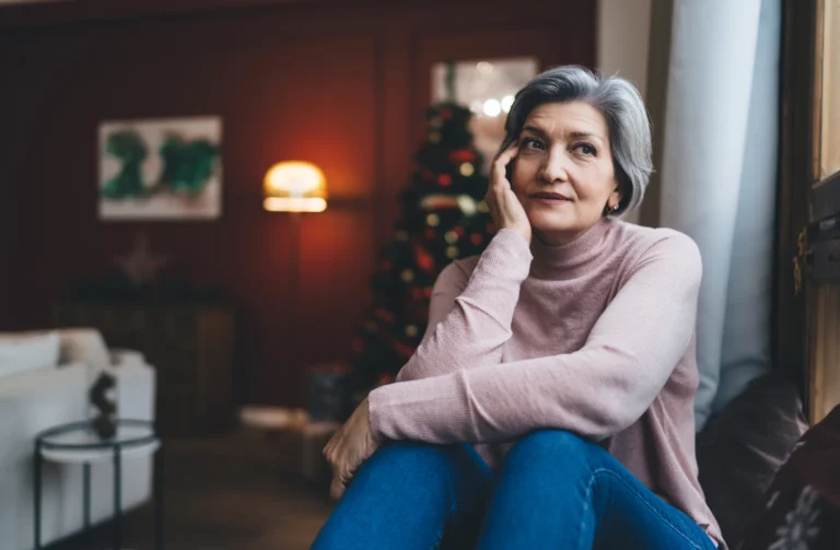 Gray-haired woman sitting at home in a pink sweater, deep in thought